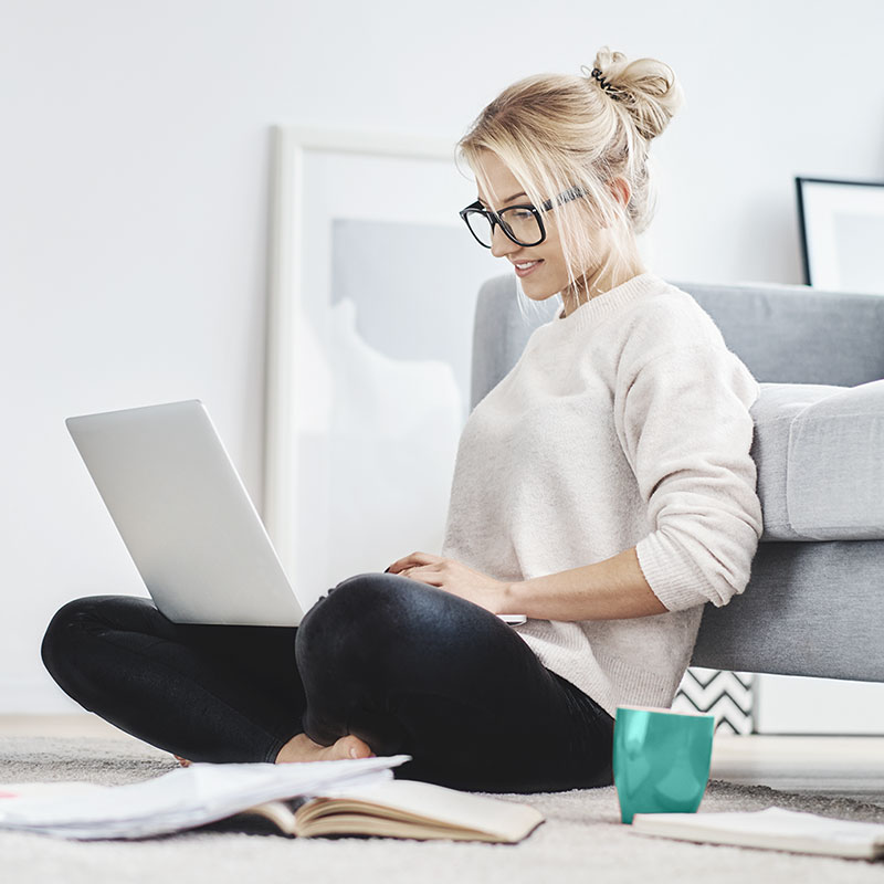 contentpic_stb-online_01 Blonde Frau Mitte 20 sitzt vor ihrem Sofa mit dem Laptop auf dem Schoß
